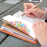 
A girl writing on midori style traveler's notebook with moody marble design on a wooden table